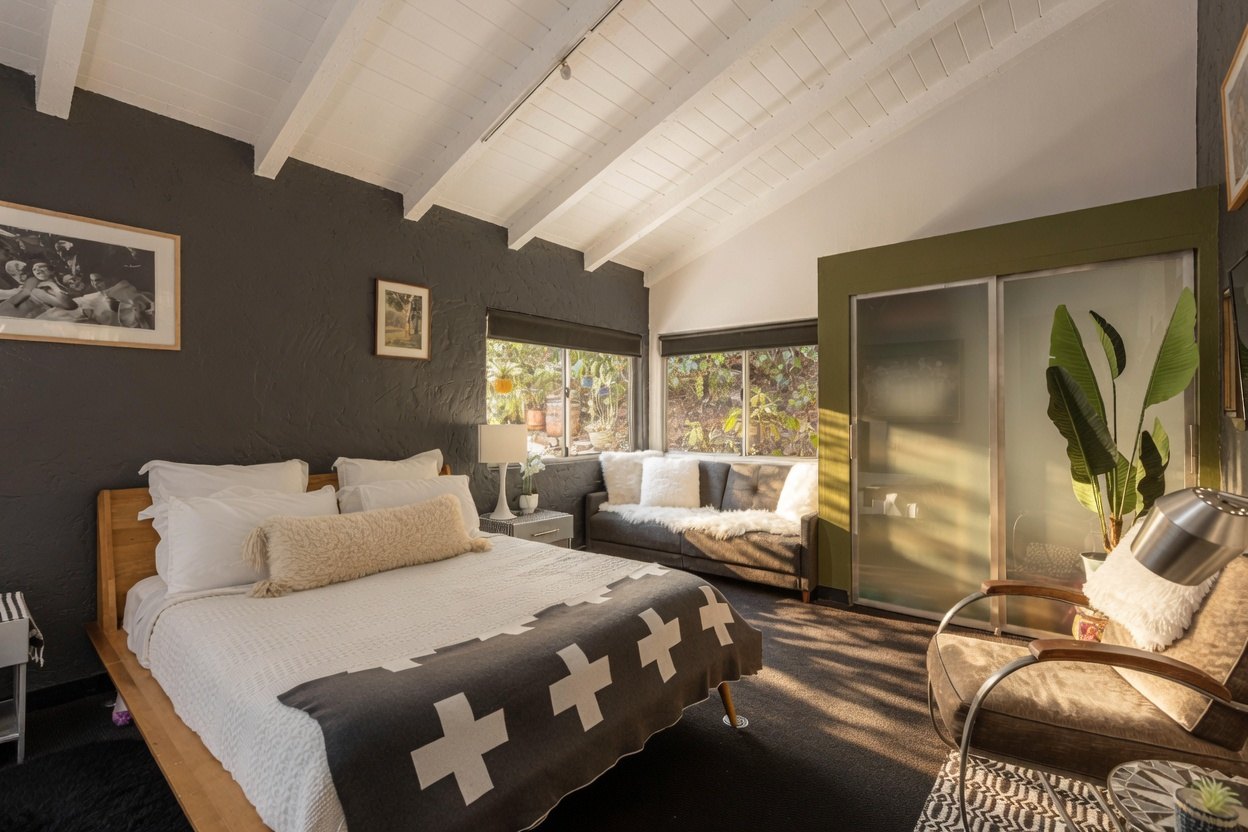 A sunlit bedroom with corner windows and a garden outlook